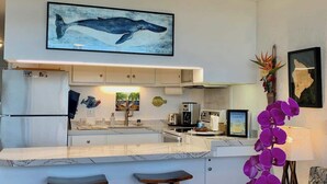 A modern kitchen with a marble countertop, white cabinets, and a large whale painting above the sink.