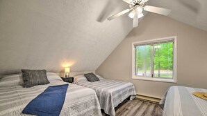 A bedroom with two beds, a ceiling fan, a window with a view of greenery, and a nightstand with a lamp. - Higgins Lake Getaway - Boating, Fish, Golf, ATV! (Roscommon)