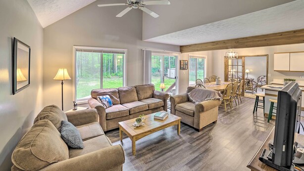 A spacious living room with a large sofa, a coffee table, and a dining area with chairs and a table. - Higgins Lake Getaway - Boating, Fish, Golf, ATV! (Roscommon)