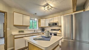 A modern kitchen with white cabinetry, a central island, stainless steel appliances, and a window providing natural light. - Higgins Lake Getaway - Boating, Fish, Golf, ATV! (Roscommon)