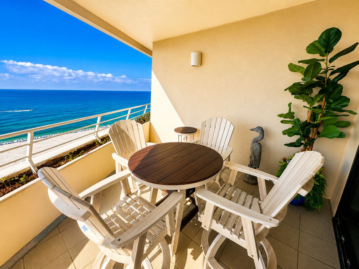 A balcony with a wooden table and white chairs, overlooking a beach and ocean.