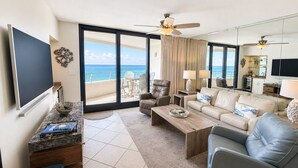 A spacious living room with a large TV, comfortable seating, a coffee table, and a view of the ocean. - Eden W 903 A remodeled beautiful 1 Bedroom 2 Bath Gulf Front Condo with Stunning Views! (Pensacola)