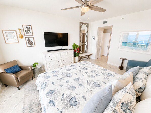 A bedroom with a bed, a TV, a ceiling fan, a dresser, a chair, and a window with a view. - Eden W 903 A remodeled beautiful 1 Bedroom 2 Bath Gulf Front Condo with Stunning Views! (Pensacola)