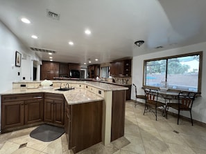 A spacious kitchen with a large island, dark wooden cabinets, and a dining area with a view through a large window.