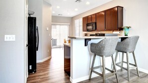A modern kitchen with wooden cabinets, a microwave, and two bar stools.