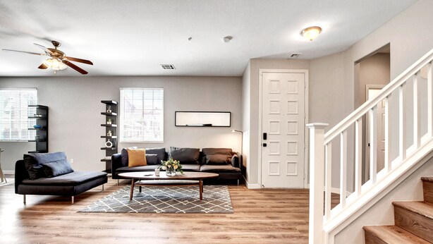 A spacious living room with hardwood flooring, a ceiling fan, a staircase, and a door leading to another room.
