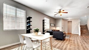 A modern living room with a dining area, wooden flooring, and a ceiling fan.