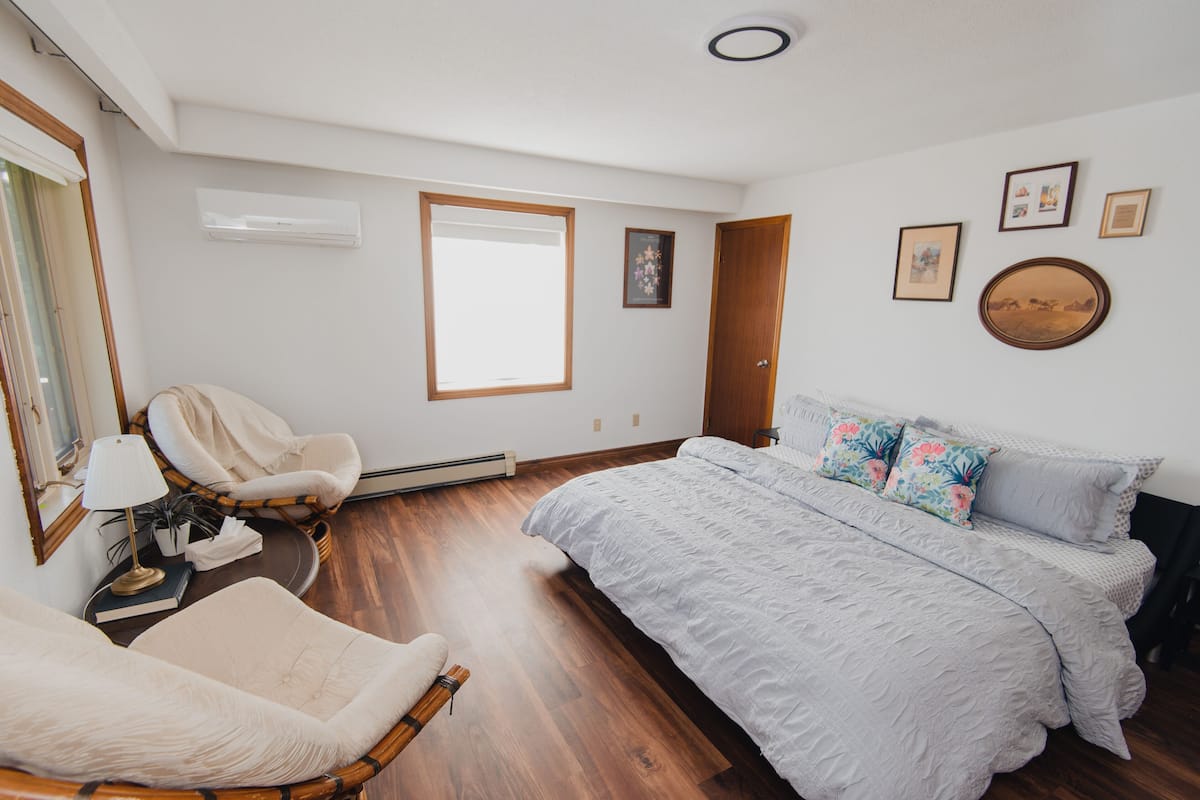 A bedroom with a large bed, a chair, a bedside table, and a window.