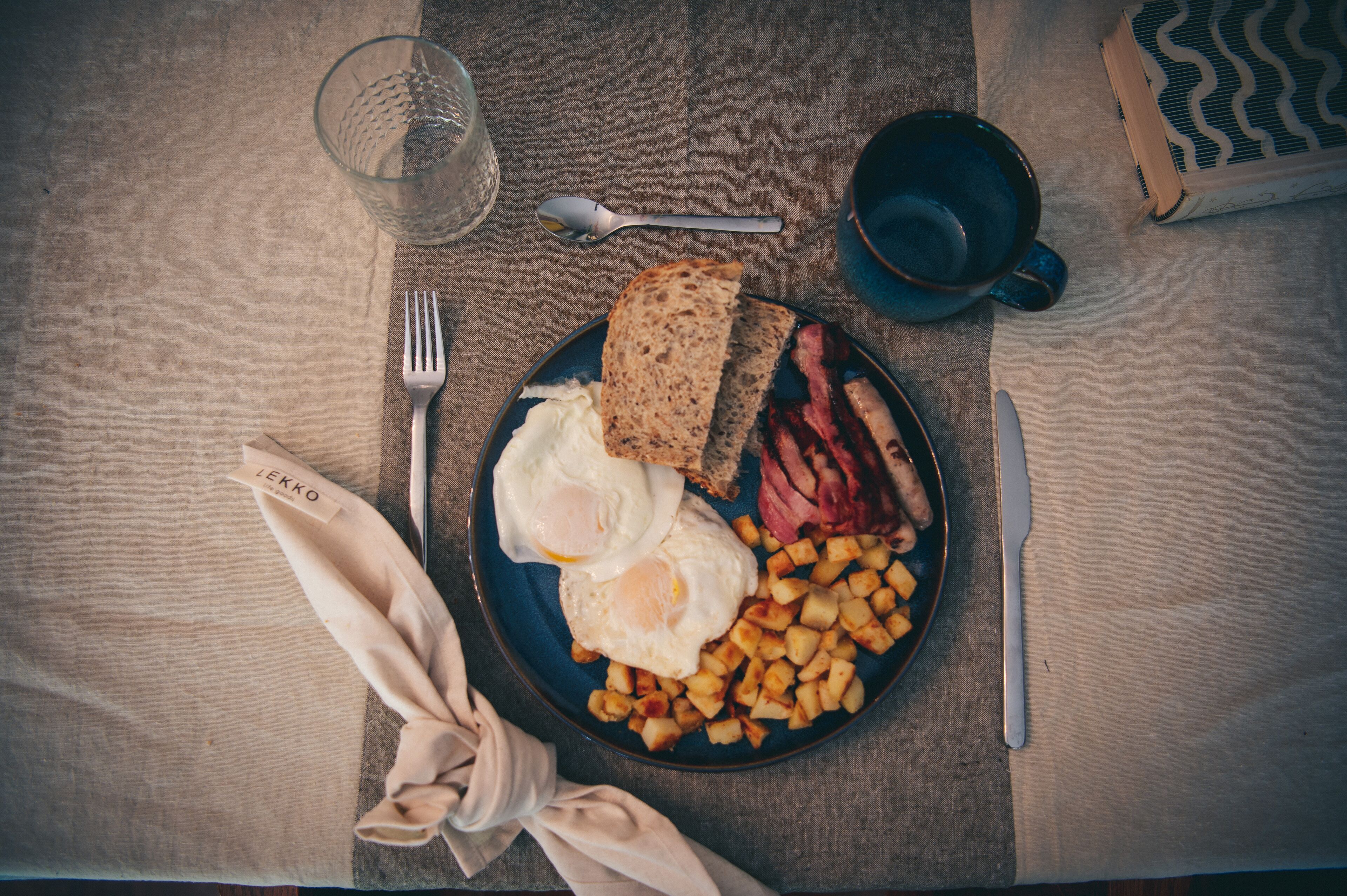 A breakfast plate with eggs, bacon, toast, and potatoes on a table.