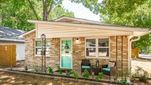 Une petite maison en briques avec une porte verte, deux fenêtres et un porche meublé de meubles en osier.
