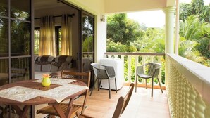 Un balcón con mesa y sillas, un sofá y un ventanal corredizo que da a un jardín.