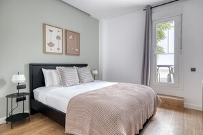 Relax in this serene bedroom with a large bed, nightstand, and artwork, offering a view of the outdoor area through a sliding door.