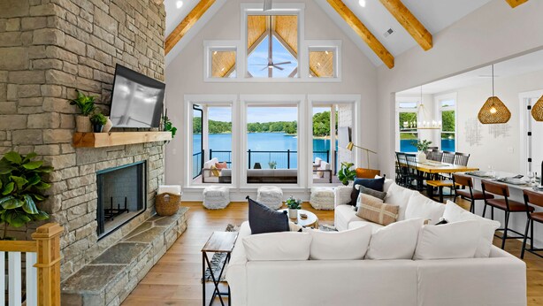 A spacious living room with a stone fireplace, a large white sofa, and a dining area with wooden furniture. - Hogan Crest w/Heated Pool & Optional Boat Rental (Mooresville)