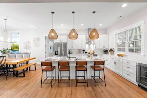 A modern kitchen with white cabinets, a central island with bar stools, pendant lighting, and a dining area with a wooden table and chairs. - Hogan Crest w/Heated Pool & Optional Boat Rental (Mooresville)