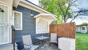 Un patio con mesa y sillas, cerca de madera, y una casa con ventana y puerta.