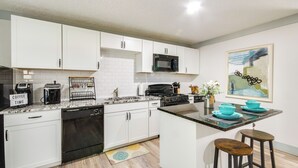 Una cocina moderna con armarios blancos, microondas, cafetera y una pequeña barra con taburetes.