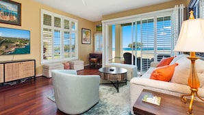 A spacious living room with a large window offering a view of the beach, a ceiling fan, and a television on a cabinet. - New Owner Special! Ocean View in KoOlina, HI (Kapolei)