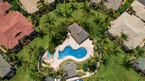 An aerial view of a residential area with a swimming pool surrounded by palm trees and houses with red roofs. - New Owner Special! Ocean View in KoOlina, HI (Kapolei)