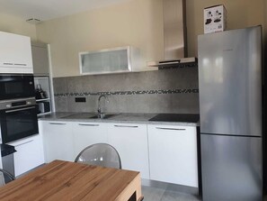 A modern kitchen with white cabinets, a stainless steel refrigerator, a microwave, and a sink.