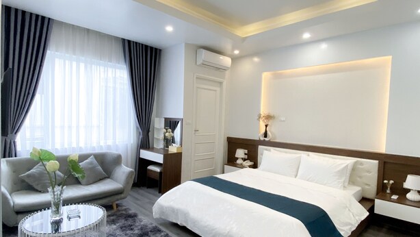 Una habitación de hotel moderna con una cama grande, un sofá, una mesita de centro redonda y un escritorio con una lámpara.