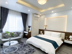 Una habitación de hotel moderna con una cama grande, un sofá, una mesita de centro redonda y un escritorio con una lámpara.