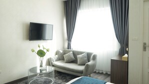 Una habitación de hotel moderna con sofá, una mesita auxiliar, televisor de pantalla plana en la pared y un amplio ventanal con cortinas.