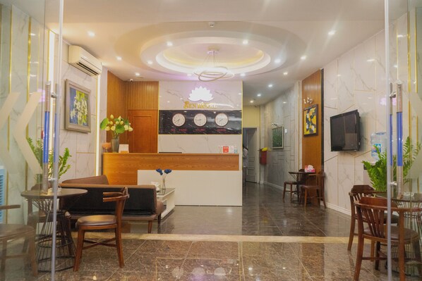 Un vestíbulo de hotel con mostrador de recepción, zona de estar y televisor montado en la pared.