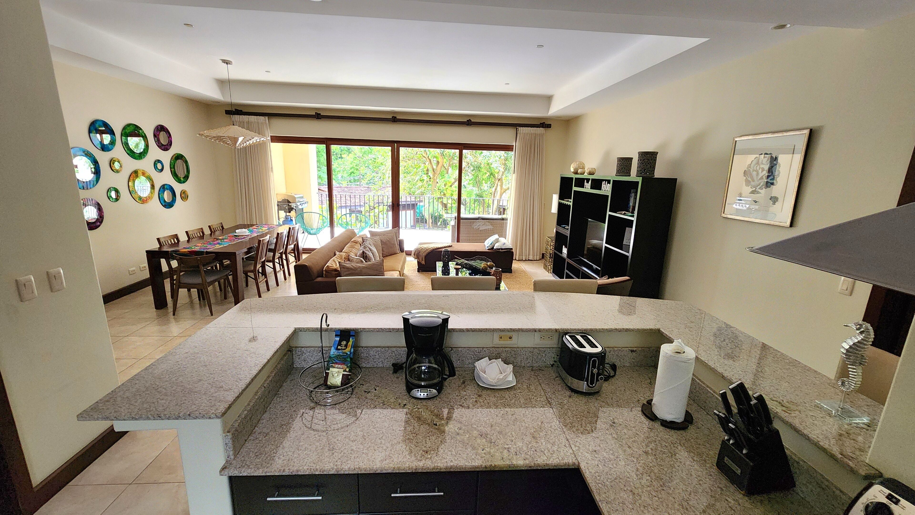 A modern kitchen with a central island, dining area with a table and chairs, and a living area with a sofa and coffee table.