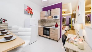 A modern kitchen with a microwave, oven, and wooden cabinets. There is a dining area with a white table and chairs. - Orange 1: Studio Apartment in St. Julian's (Swieqi)