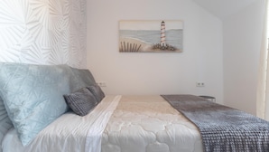 A bedroom with a bed, pillows, a blanket, a painting of a lighthouse, and a textured wall. - ATICO CASTILLO - Fantastic apartment with sea views and free WiFi. (Fuengirola)