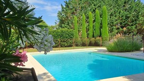 Een zwembad met helderblauw water, omringd door groen en een stenen muur.