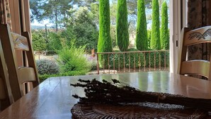 Een houten tafel met een geweven placemat en een decoratieve tak. Een metalen leuning en groen zijn zichtbaar door een open deur.