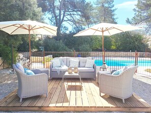 Un espace extérieur aménagé avec des meubles en osier et des parasols, donnant sur une piscine.