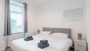 Habitación de hotel con una cama grande, una mesita de noche con lámpara y una ventana con cortinas.