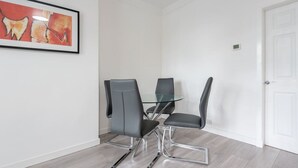 Una habitación moderna con una mesa de vidrio y cuatro sillas grises, paredes blancas y una puerta.