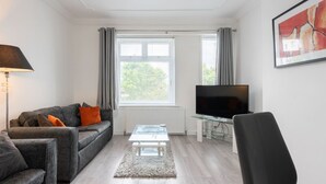 Un salón moderno con un sofá gris, una mesa de centro de vidrio, un televisor negro y un cuadro enmarcado en la pared.