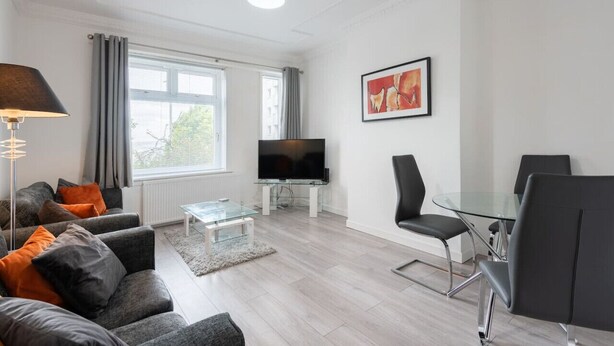 Una sala de estar moderna con un sofá, una mesa de centro, televisor y una mesa de comedor de vidrio con sillas.