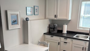 Een keuken met witte kastjes, een koffiezetapparaat, een spoelbak en een eettafel met stoelen.