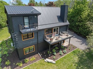 A modern two-story house with a balcony, a covered patio, and a chimney.