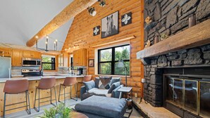 Interior de una cabaña de madera con cocina, comedor y chimenea.