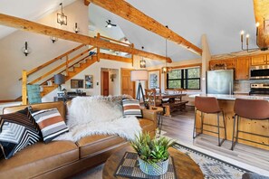 A spacious living room with a high ceiling, exposed wooden beams, a cozy fireplace, and a dining area with a large window. - Newly Updated Log Home on 5 acres - The Great Escape (Sister Bay)