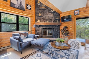 A cozy cabin interior with a stone fireplace, wooden walls, a large window, and a comfortable seating area. - Newly Updated Log Home on 5 acres - The Great Escape (Sister Bay)