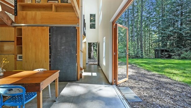 Un interno moderno con una scala in legno, una sala da pranzo e vista su una foresta.