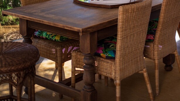 Une table à manger en bois, des chaises en osier, un luminaire suspendu et une vue sur l’extérieur grâce à une porte vitrée.