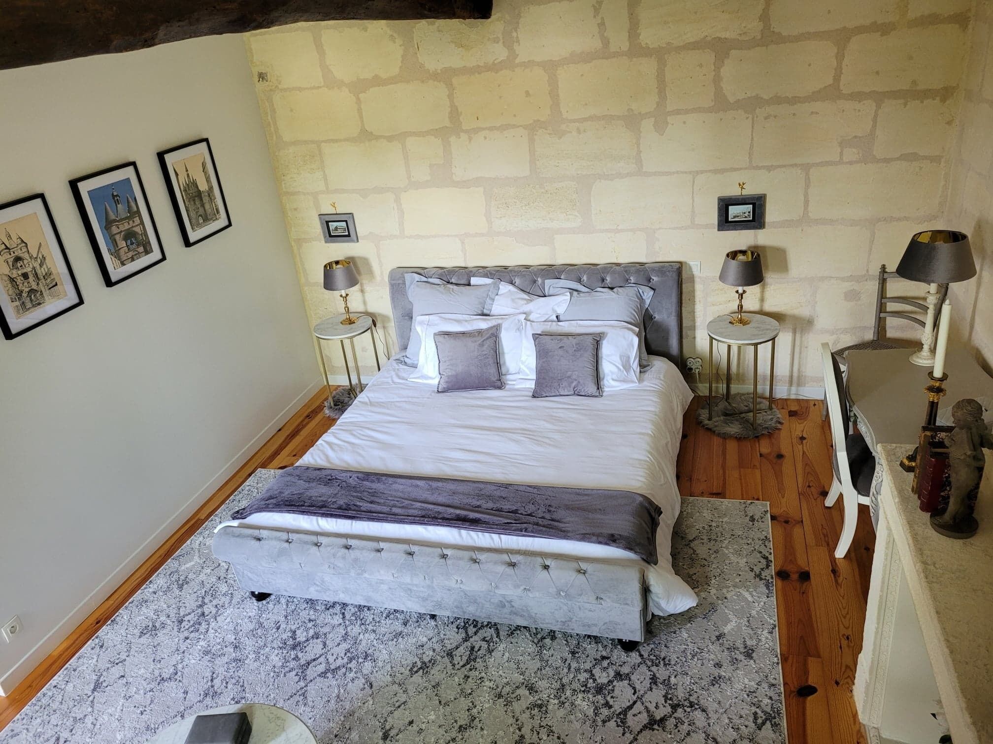 A bedroom with a large bed, two bedside tables, a chair, and a stone wall.