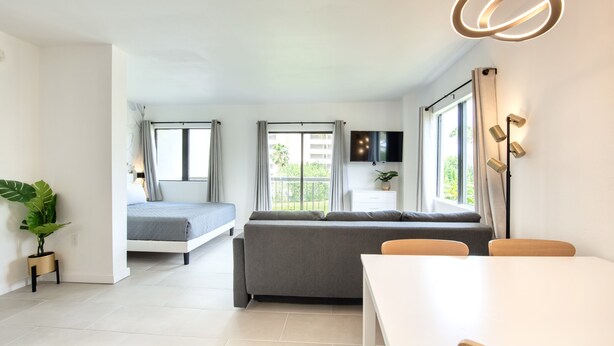 A modern living room with a sofa, a dining table, and a TV mounted on the wall. - Lovely Studio near Universal Studios (Orlando)
