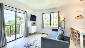 A modern living room with a grey sofa, a flat-screen TV, a dining table with chairs, and large windows with curtains. - Lovely Studio near Universal Studios (Orlando)