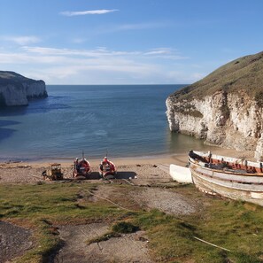 A coastal scene with cliffs, a beach, and boats. - Seaside Cottage Hot tub & Games Room (Bridlington)