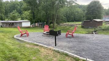 Une terrasse en gravier avec deux chaises Adirondack rouges, une boîte aux lettres et un abri en bois, le tout situé dans un cadre rural.