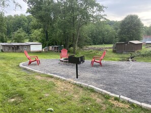 Une terrasse en gravier avec deux chaises Adirondack rouges, une boîte aux lettres et un abri en bois, le tout situé dans un cadre rural.